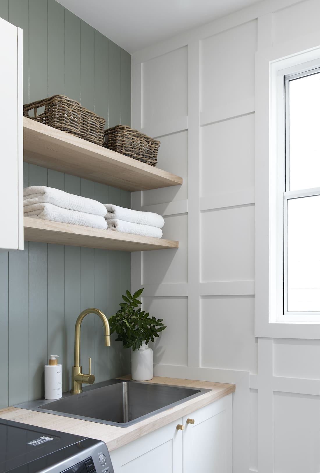 Green panelled wall in laundry with open shelving