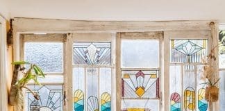 Ivy De Bruijn, the artist behind Ivy's Glass Cottage in front of stained glass art