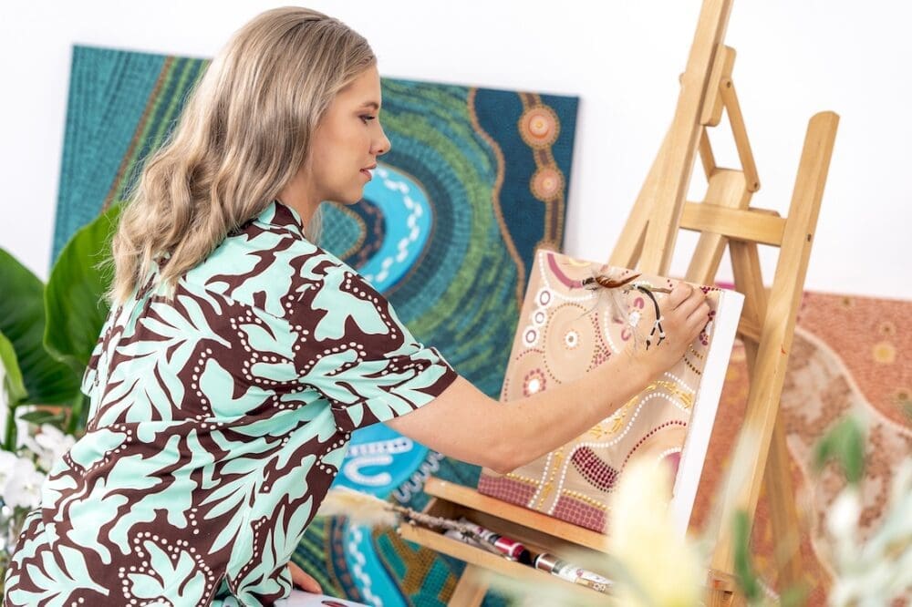 Domica Hill Indigenous artist behind By Meeka painting at easel