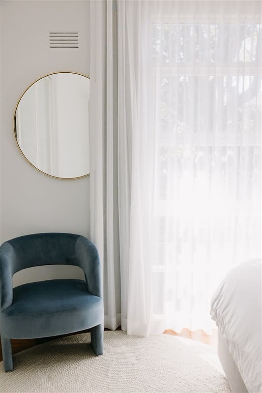 Blue occasional chair in corner of bedroom with sheer curtains and mirror